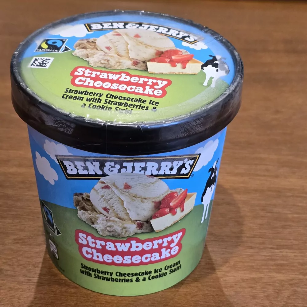 A pint of Ben and Jerry's Strawberry Cheesecake ice cream on a wooden table