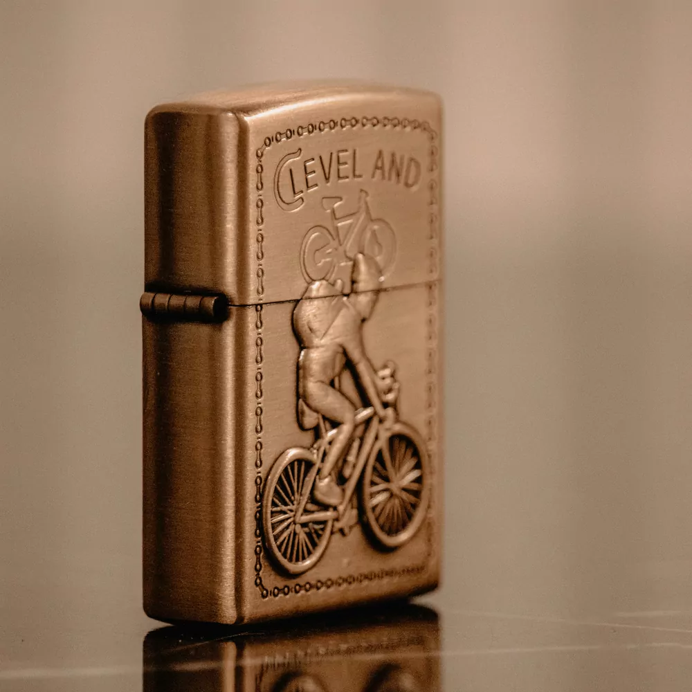 A brass flip lighter embossed with a cyclist, on a reflective surface